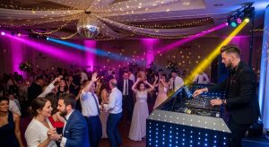 Wedding DJ performing at a lively reception with guests dancing and colorful lighting