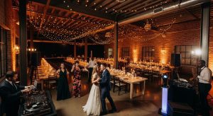 A dramatic wide-screen scene showcasing a stylish Surry Hills wedding reception inside a modern urban venue. Warm romantic lighting, exposed brick walls, contemporary décor, guests dancing and celebrating, a professional DJ setup with subtle live entertainment elements, candlelit tables and soft uplighting, cinematic depth capturing the sophistication and creative energy of Surry Hills weddings.