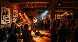A dramatic wide-screen scene of a stylish Surry Hills event space featuring live musicians performing on a small stage. Warm atmospheric lighting, exposed brick walls, modern urban décor, guests mingling with drinks, a guitarist and vocalist illuminated by soft spotlights, artistic inner-city ambience, realistic cinematic photography style capturing the creative energy of Surry Hills.